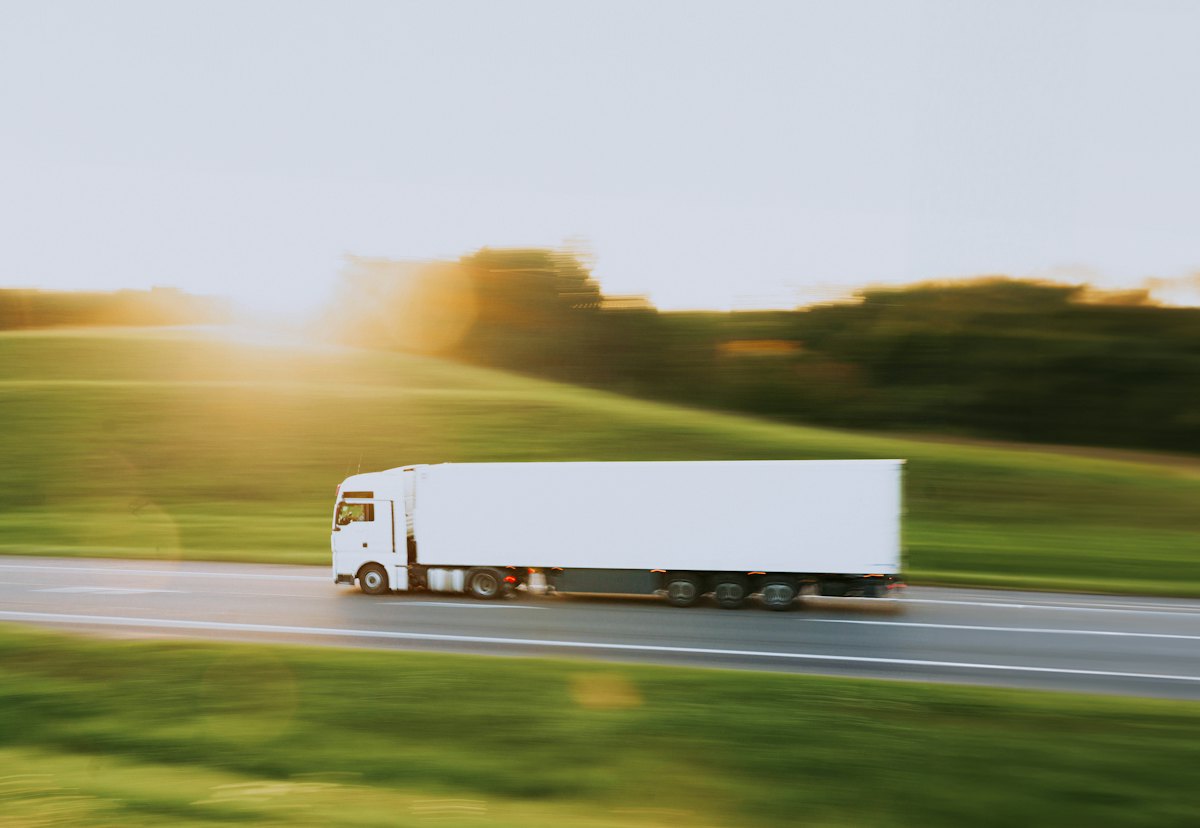 White semi-truck and trailer driving down a rural road at sunset